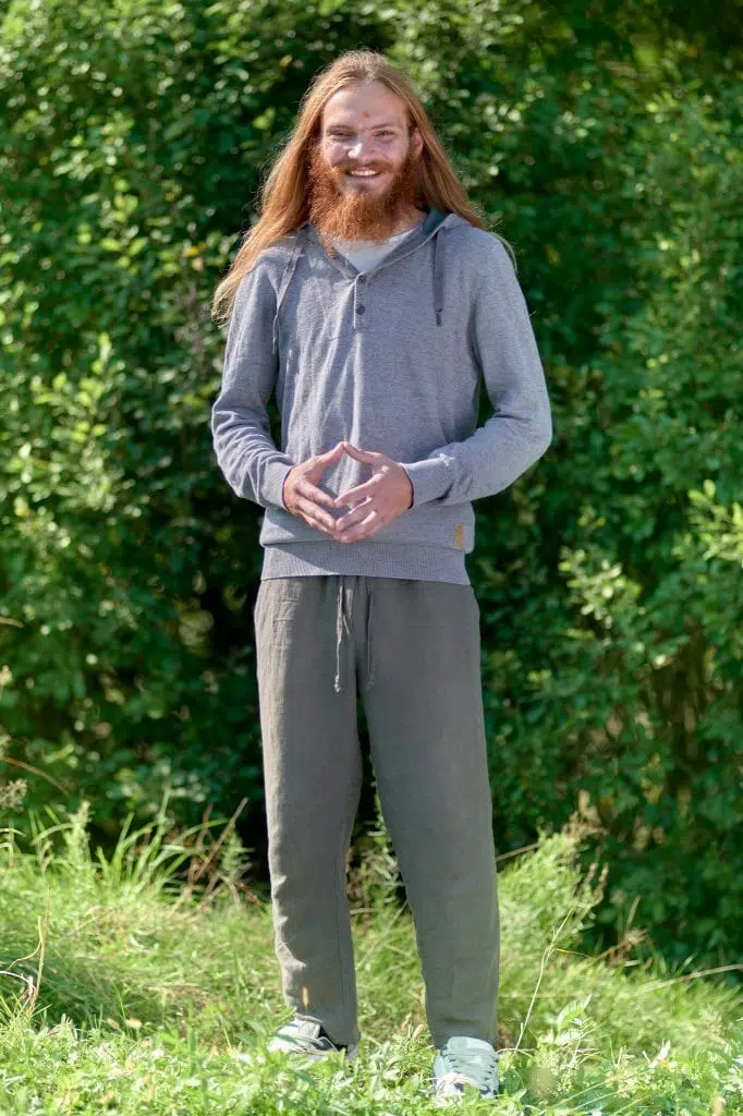 Mężczyzna szczerze uśmiechający się na tle drzew, ręce złożone w hakini mudrę - uwalnianie emocji